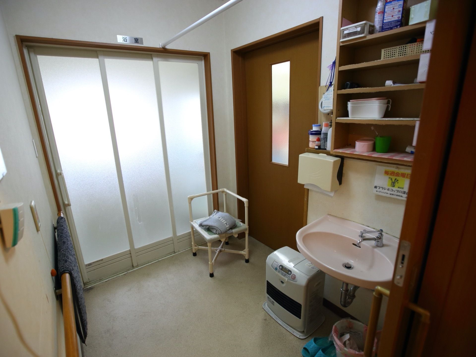 脱衣所には洗面台が設置され、ペーパーホルダーが壁に取り付けられている。足元には、ファンヒーターが置かれている。