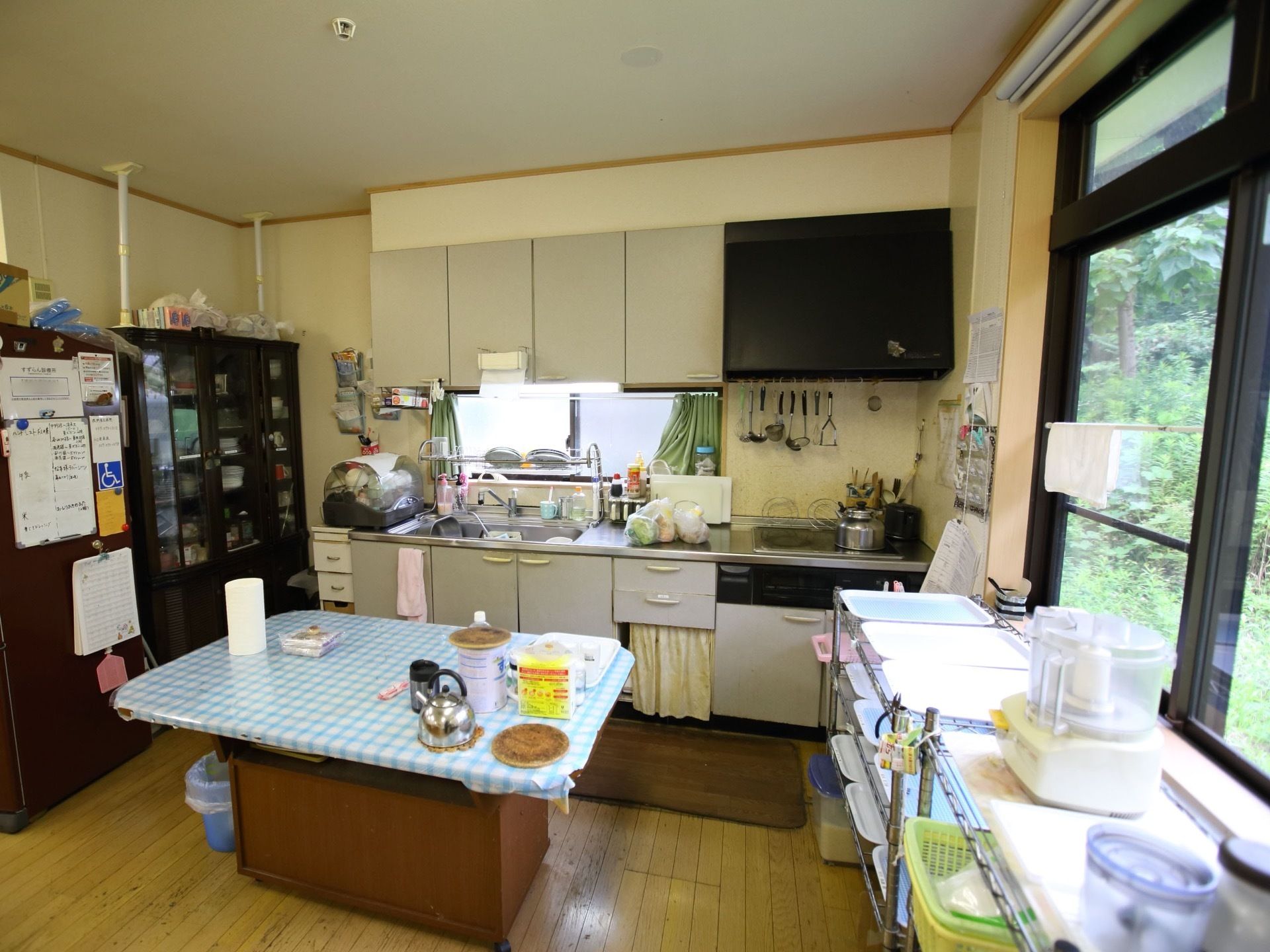 白を基調としたキッチンである。中央には机、壁際にはキッチンと黒色の棚が置いてある。調理器具は揃えられている。