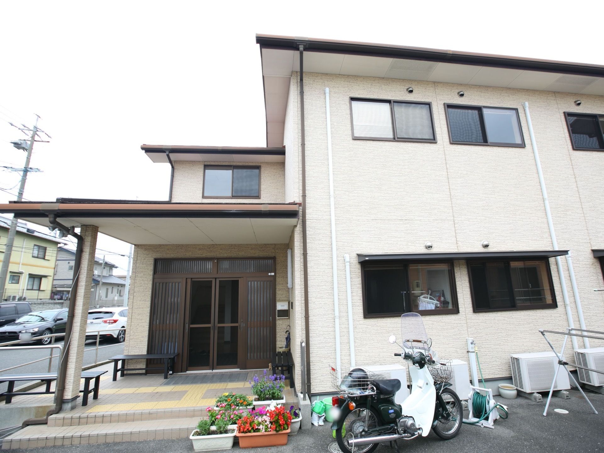 クリーム色の外壁で、２階建ての建物である。窓が多く設けられている。玄関の前には、鉢植えが４つほど置かれている。