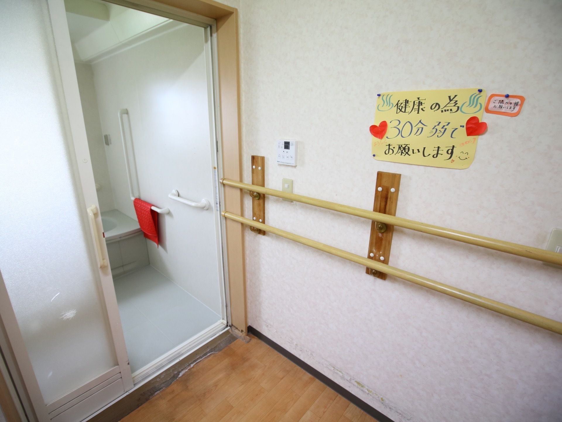 白を基調とした清潔感のある浴室である。浴室の前の通路には、壁に沿うように２段の手すりが設けられている。