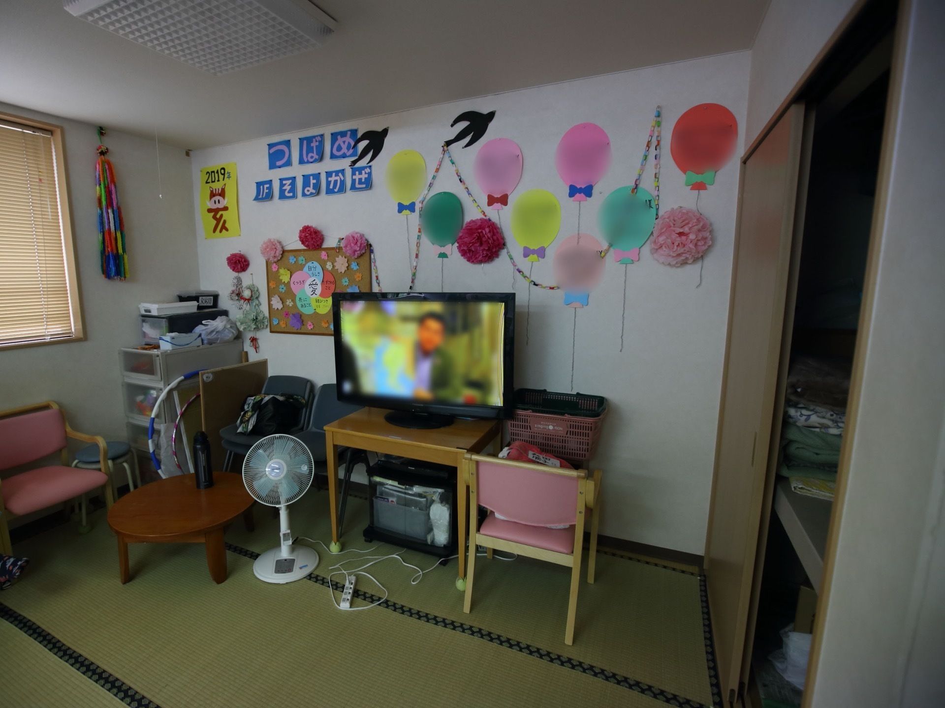 白い天井と壁に、畳の床の居室である。テレビや扇風機が備え付けられている。壁は折り紙で飾り付けられている。