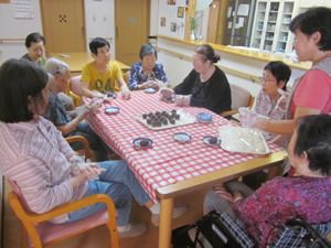 スタッフや入居者様が集まって、おやつ作りをしている。テーブルにはギンガムチェックのテーブルクロスが掛けられている。