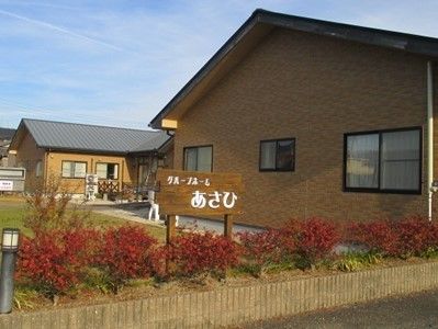 敷地周りに植栽がされており、白い文字で施設名が描かれた木の看板が立っている。広い庭があり、平屋建ての建物が建っている。