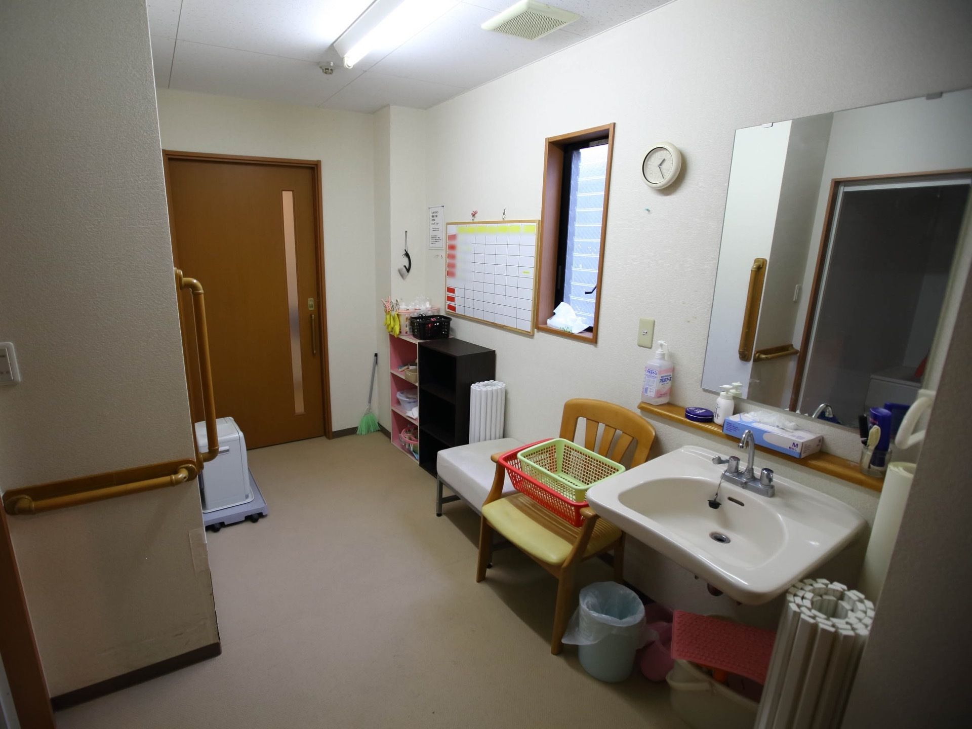 広々とした脱衣室である。洗面台や手すりが完備されており、椅子やカラーボックスが置かれている。ヒーターが壁際に設置されている。