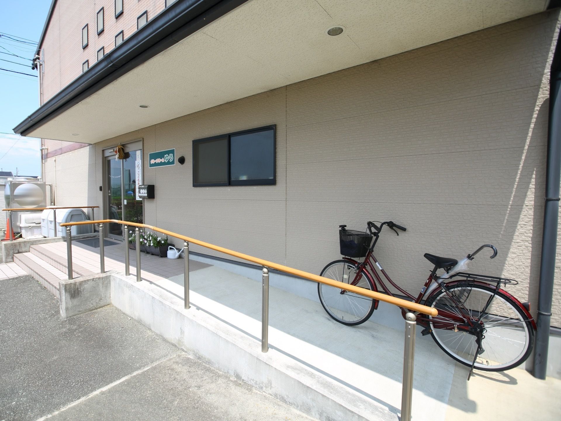 横長のひさしが設置されたエントランスである。手すり付きのスロープと階段が設けられている。プランターが壁際に置かれている。