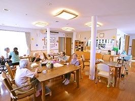 あたたかみあるフローリングのスペースといす、テーブル、そこに集う人々が写っている