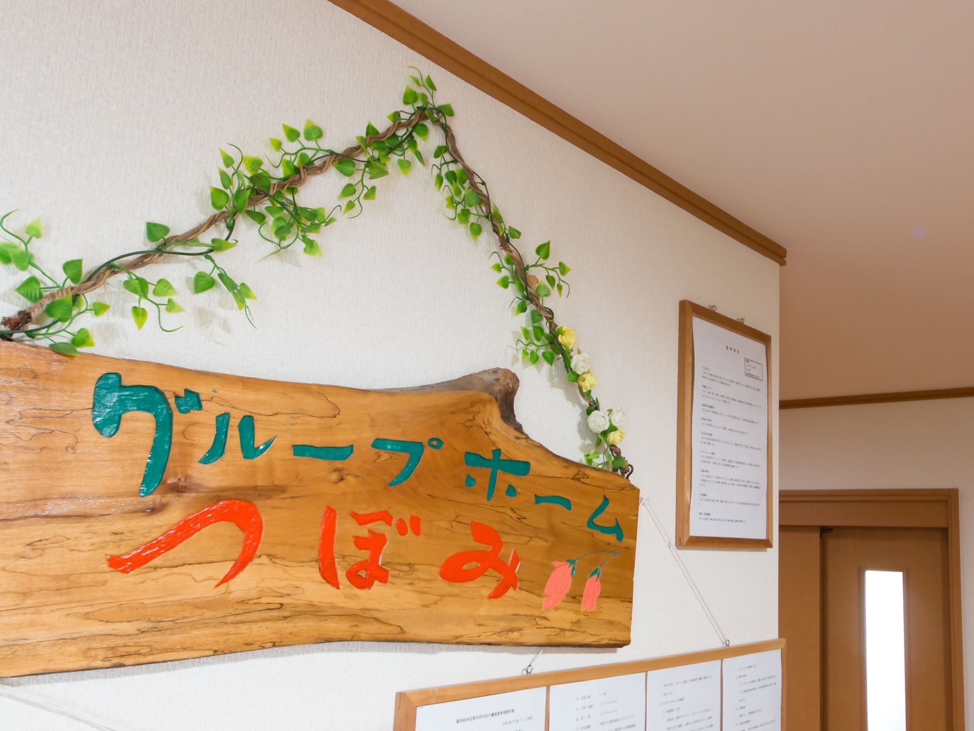 木で作られた重厚感のある施設名のプレートである。ひもの部分にはお花などを配置しており、明るい雰囲気になっている。