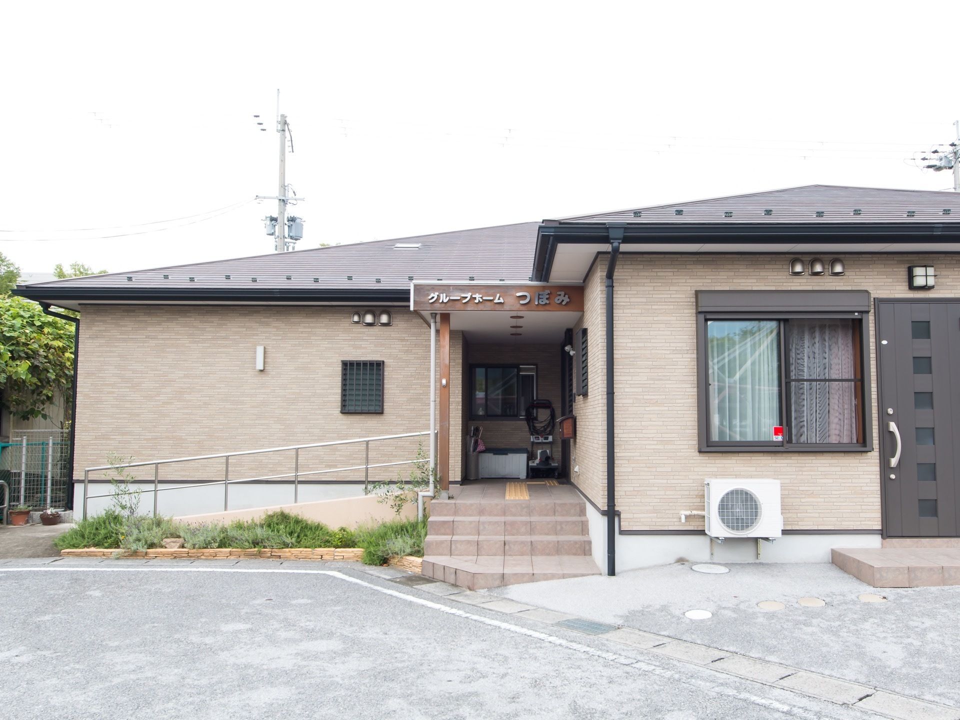 玄関までの通路は、階段と手すり付きのスロープ両方がある。施設は平屋建てで、ダークブラウン色の外観である。