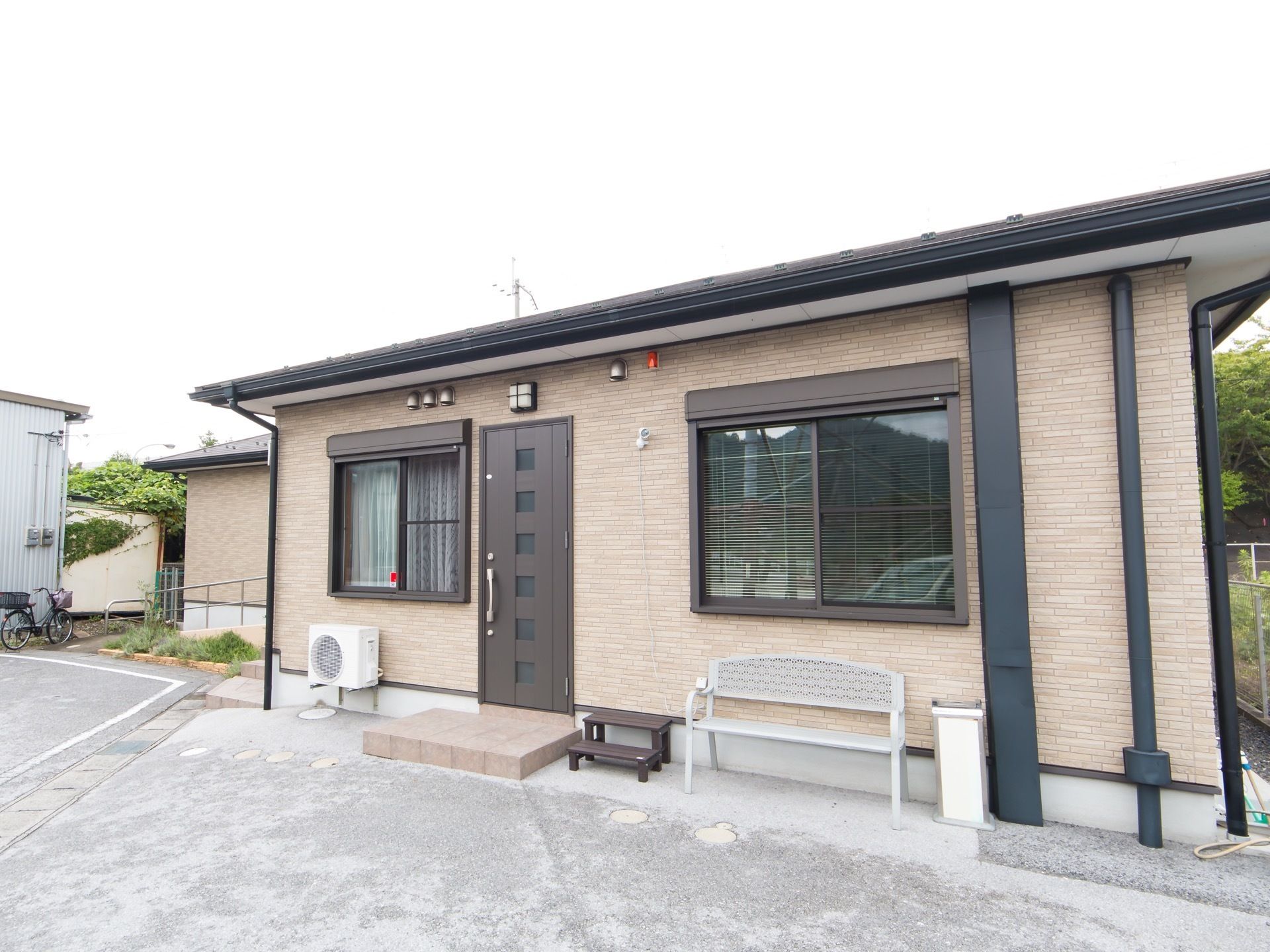 ブラウン色の施設の建物の前に白いベンチがある。ゆったりと自由に座ってくつろぐことができる。