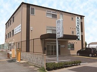 駐車スペースがある３階建ての建物はブラウン系で、敷地内にはホーム名が書かれた看板も立っている。