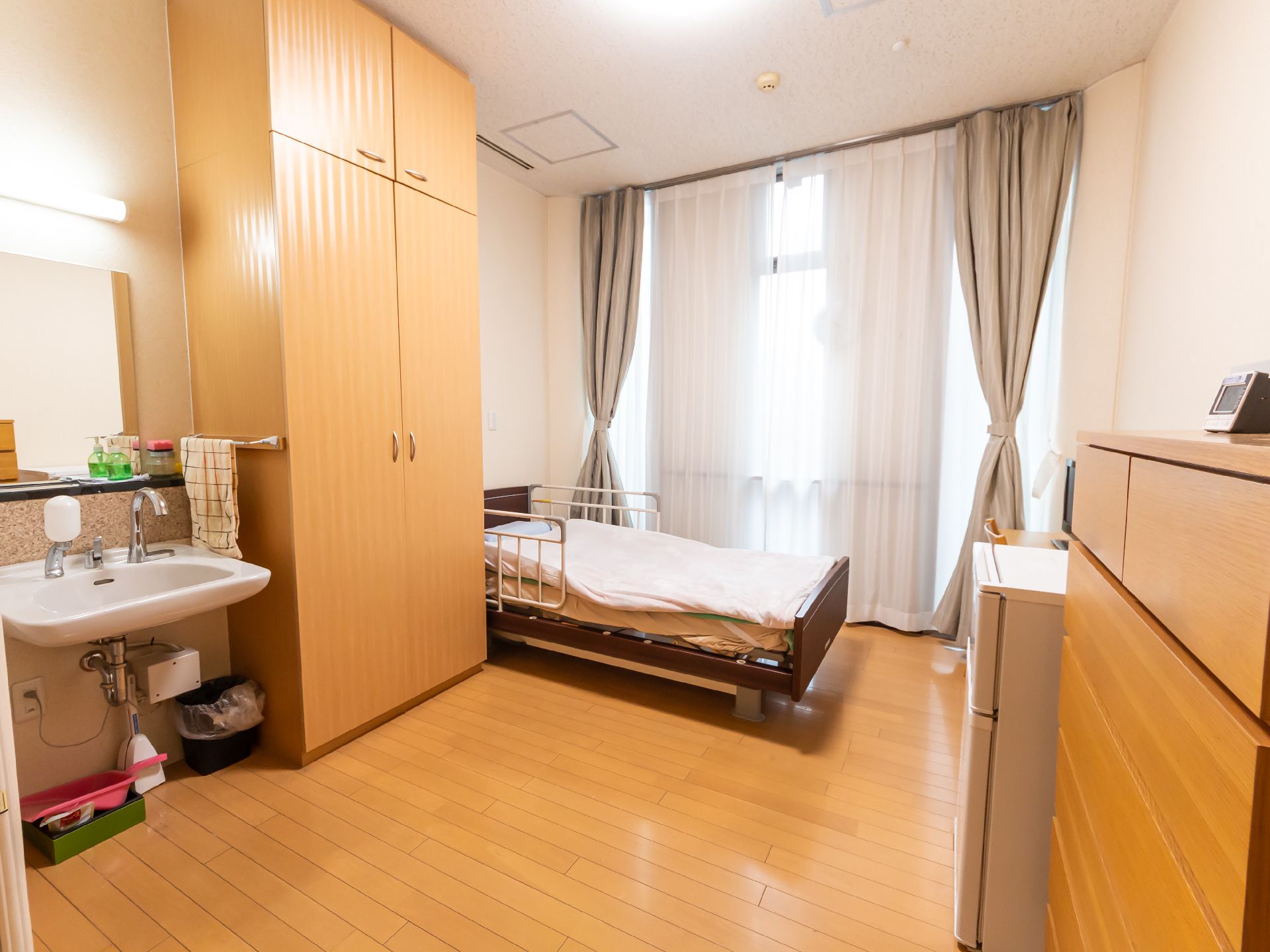 緑の多い屋外で車いすの高齢女性に付き添い笑顔で対応しているエプロンを付けた女性スタッフ。