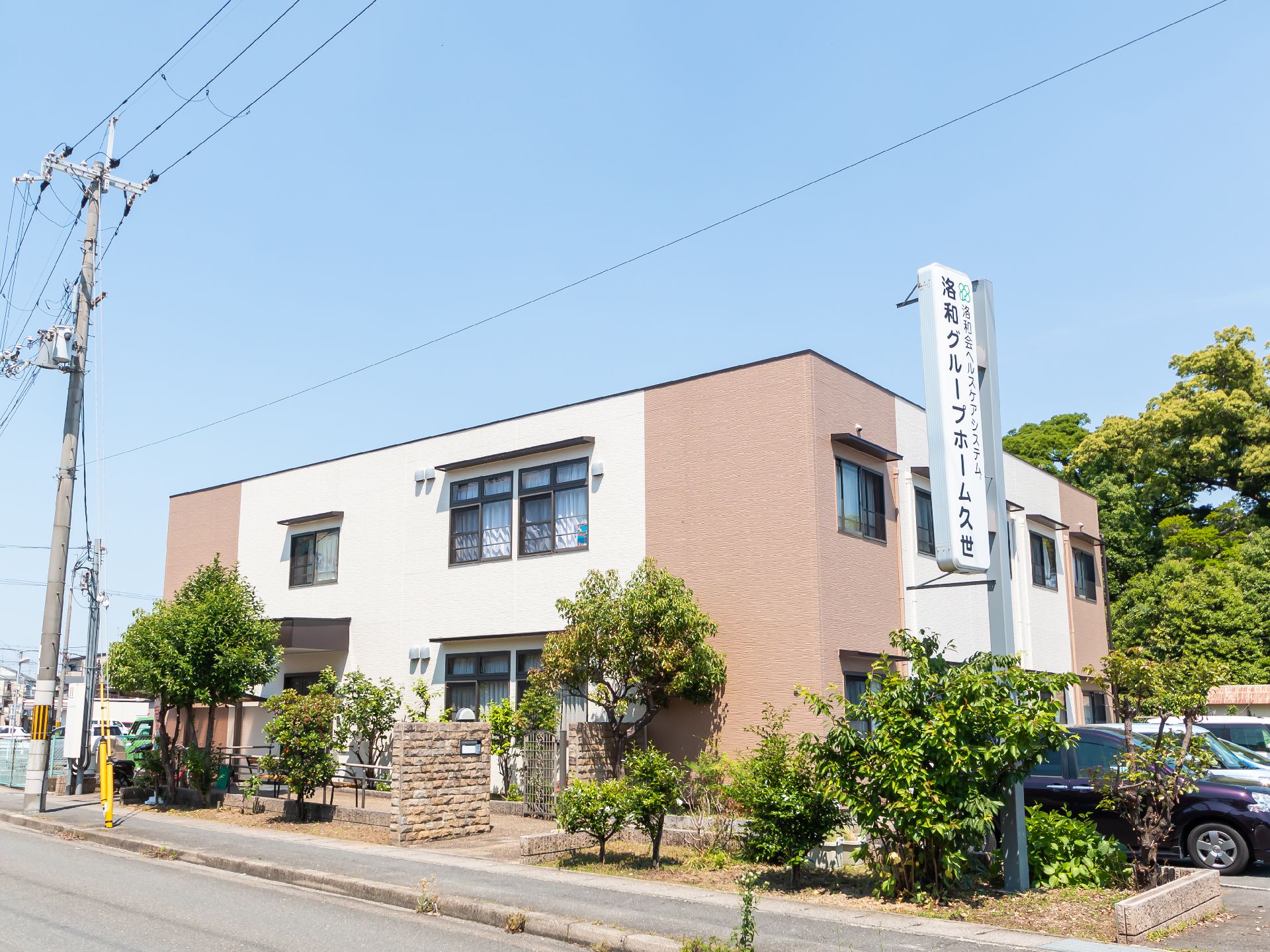 大きな駐車場がある2階建ての建物はブラウン系で、建物の玄関には屋根が付いている。