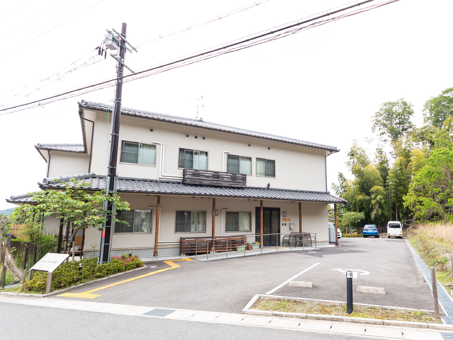緑に囲まれた場所に建っている2階建ての建物は瓦屋根が付き和の雰囲気。玄関には手すり付きのスロープもある。