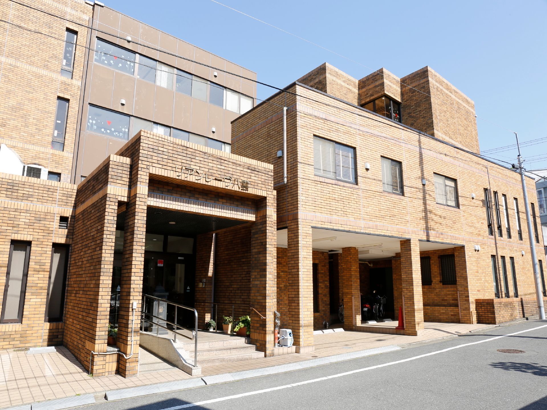 レンガ調の外観。玄関の入口は、階段のある部分と段差のない部分に分かれている。その間には、手すりが設置されている。