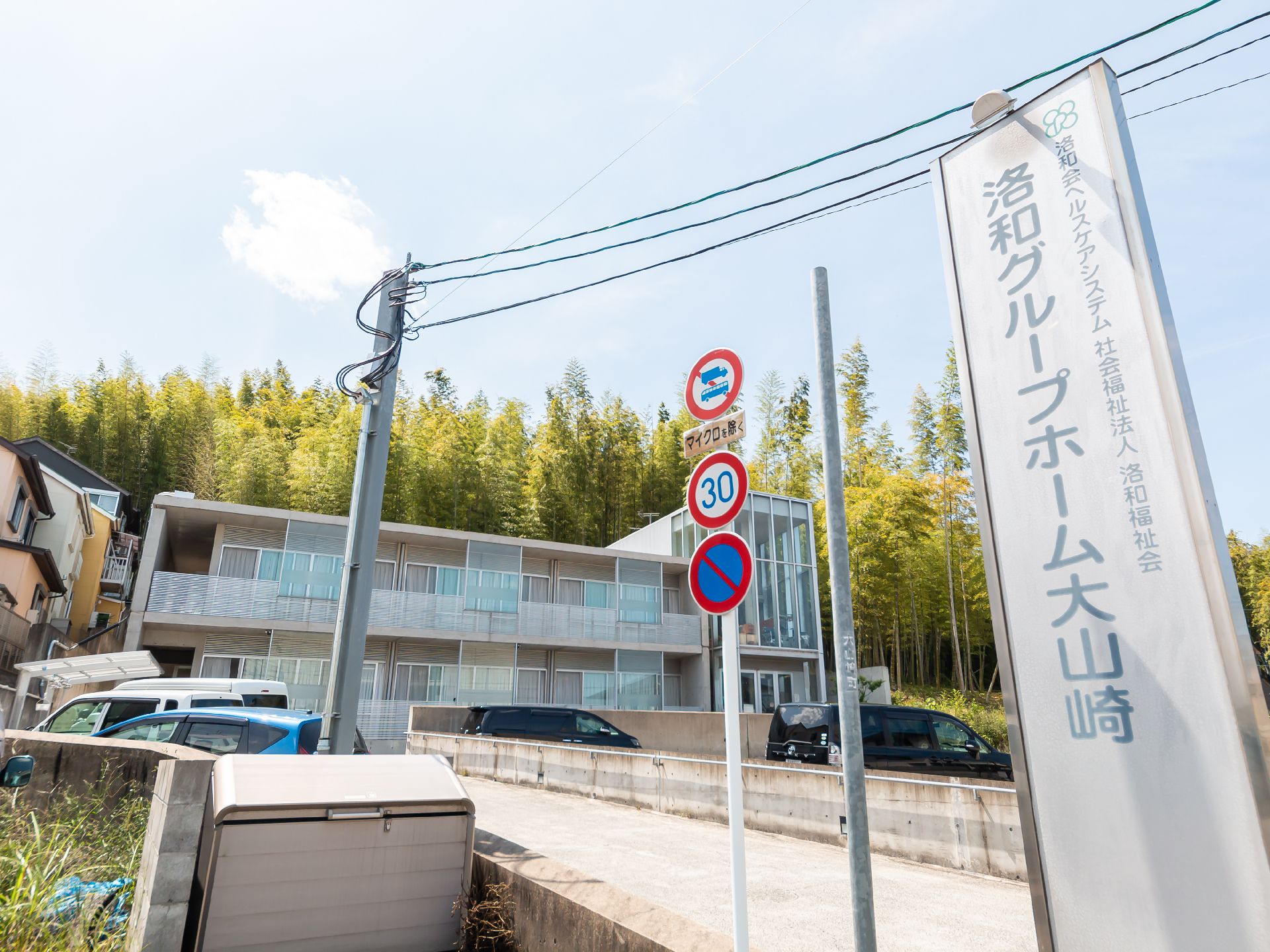 グレーの建物と敷地の入り口に立てられたホーム名が書かれた看板