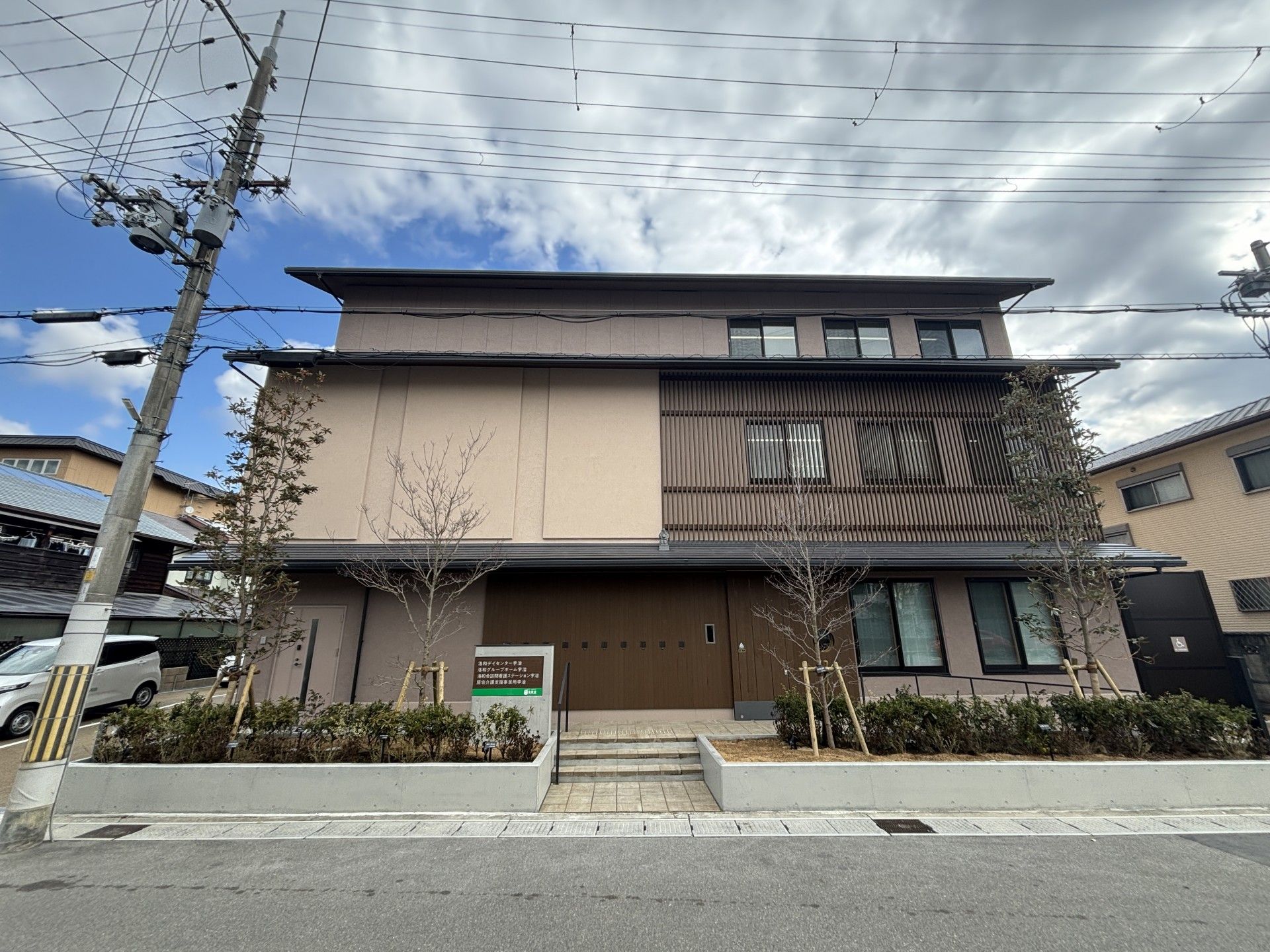 3階建てのブラウン系の大きな建物の上にはホーム名が書かれた看板が立っている。周りには緑も多い。