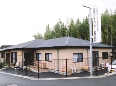 周辺に自然が多く残る場所に建てられた平屋建ての建物の玄関には屋根が付き、手すり付きのスロープが設置されている。