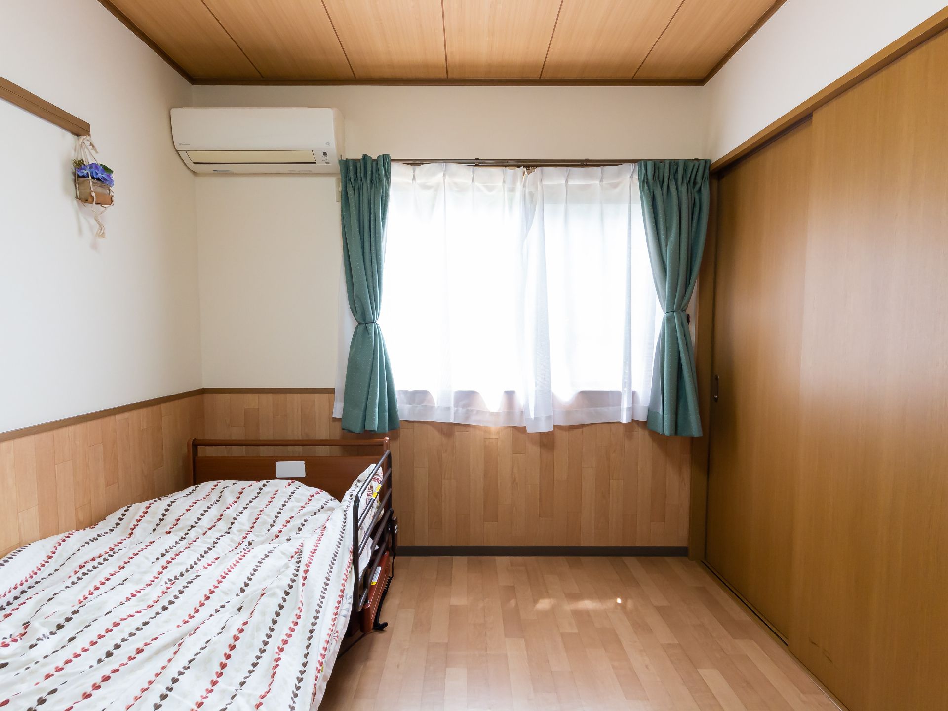 屋外で笑顔で散歩をしている車いすの高齢女性と付き添いのピンクのエプロンを付けた若い女性スタッフ。
