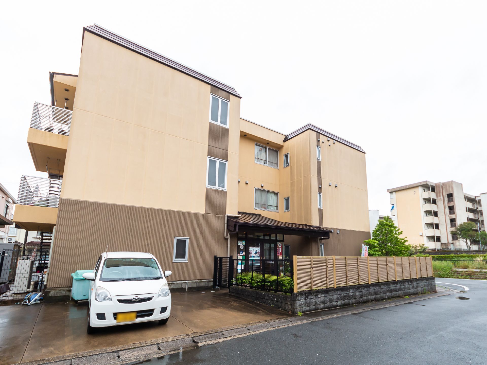 3階建ての茶色い建物と駐車場に停まっている車
