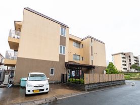 3階建ての茶色い建物と駐車場に停まっている車
