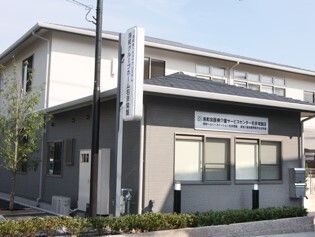 ホーム名が書かれている外壁は白とグレー。2階建ての建物の周りには草木も植えられている。