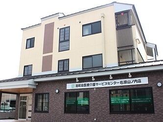 3階建ての建物の玄関には屋根が付いている。ベージュとブラウンの外壁で落ち着いた雰囲気。