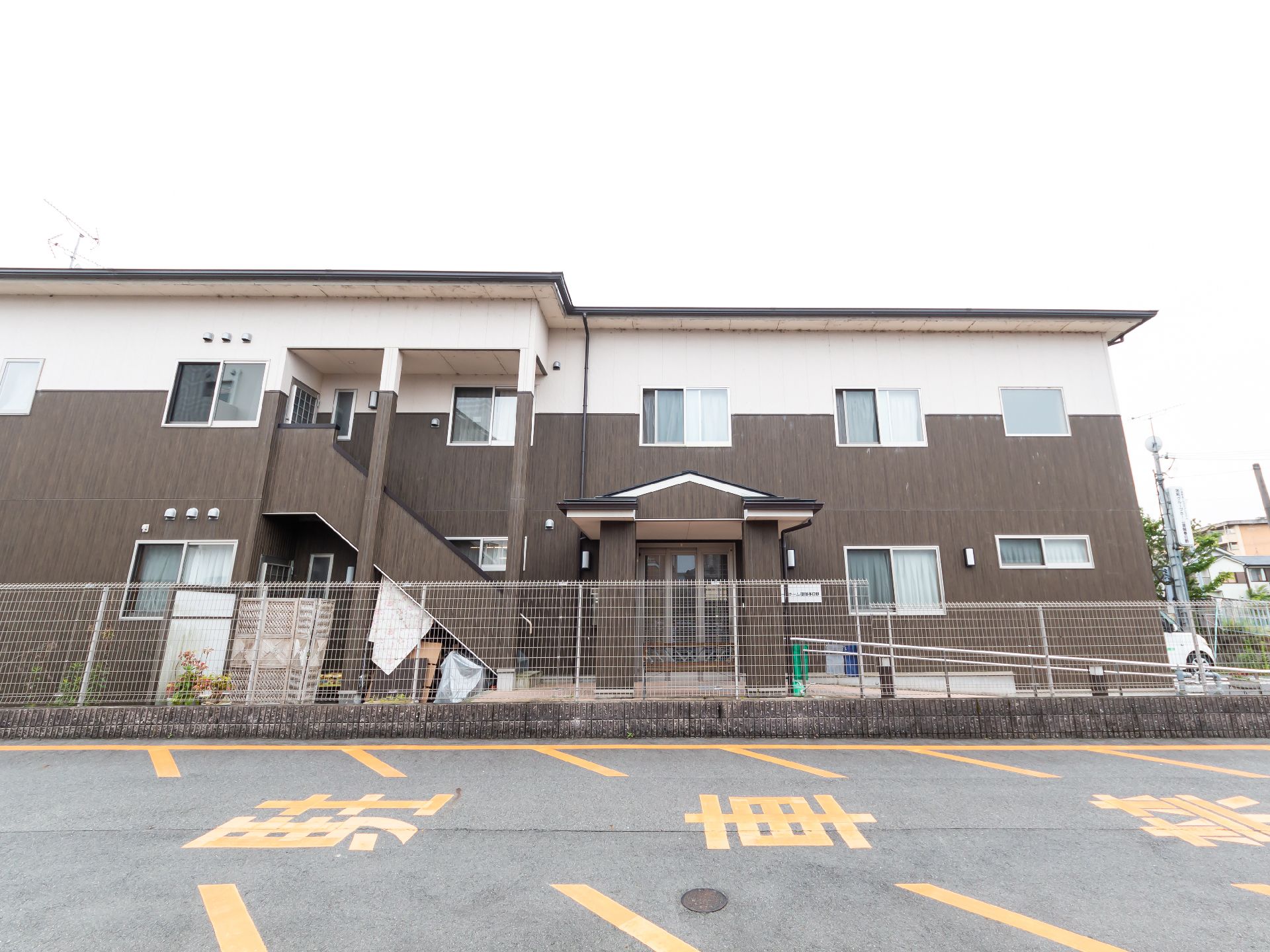 2階建ての建物の玄関には屋根が付いている。手すり付きのスロープもあり、ブラウンとベージュの2色使い。