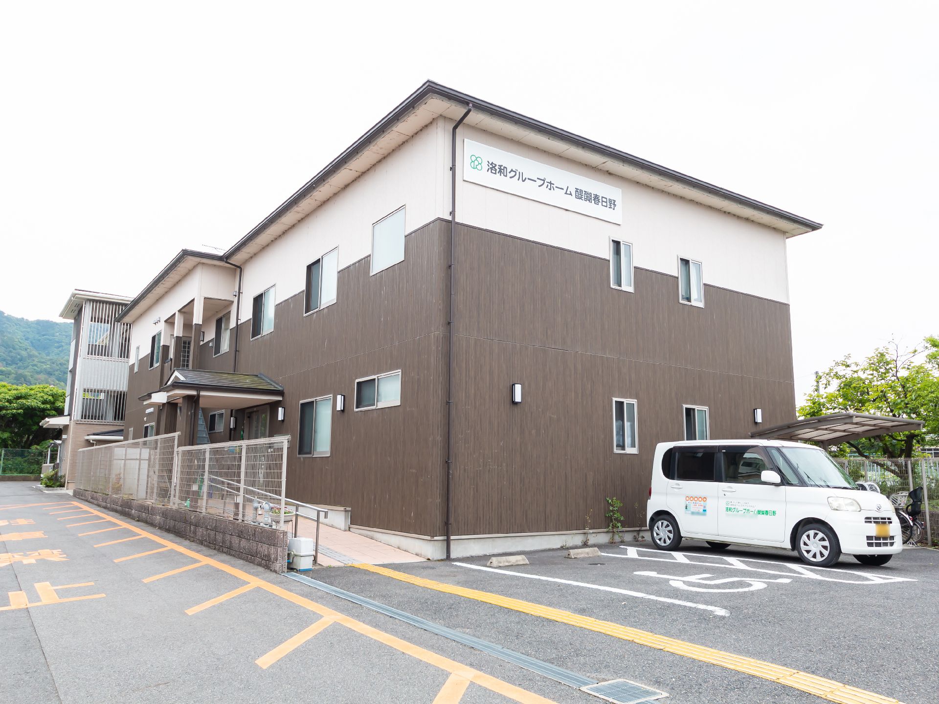 ブラウンとベージュの2階建ての建物の玄関には屋根と手すり付きのスロープが付いている。