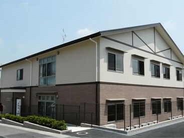 2階部分が白、1階部分がブラウンの2階建ての建物は玄関には屋根が付いている。日当たりのいい場所。