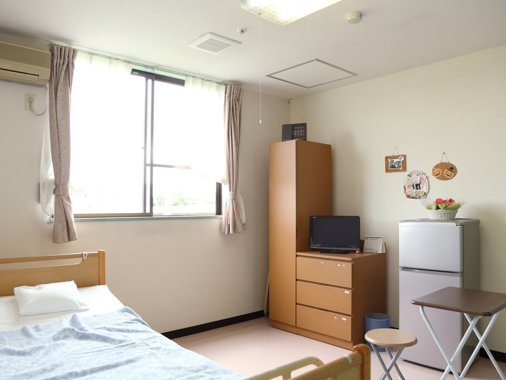 明るく広々とした居室には、介護用ベッドやエアコン、洋服タンス、液晶テレビ、冷蔵庫など必要最低限揃っている。