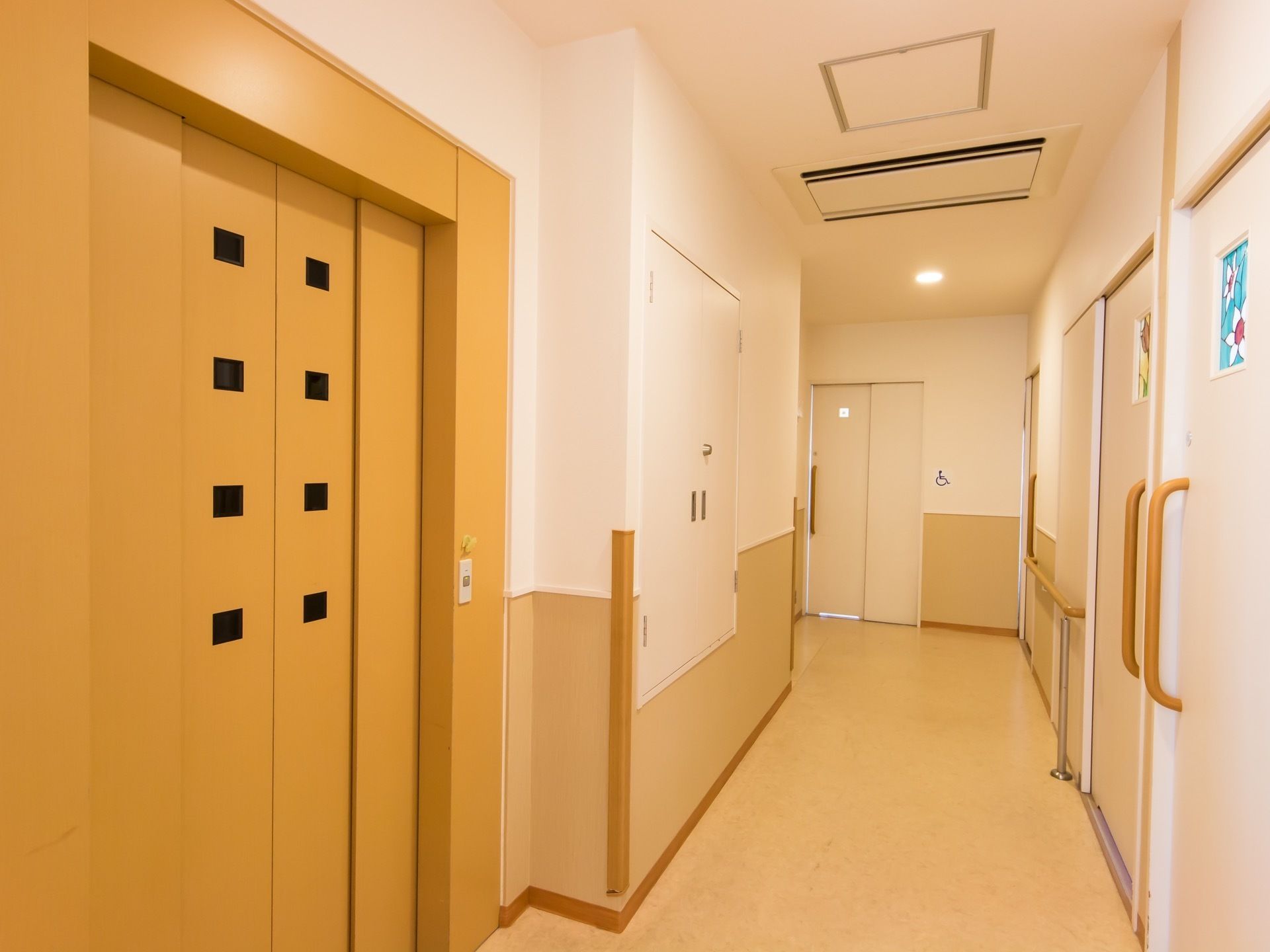 廊下にエレベーターのドアがある。ボタンが１つの操作しやすい設計である。ドアには、小窓が８つ付いている。