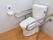 白い壁の清潔感のあるトイレである。便座の両横にステンレス製のU字型の手すりがある。洗浄便器の操作盤は右手の壁に取り付けてある。