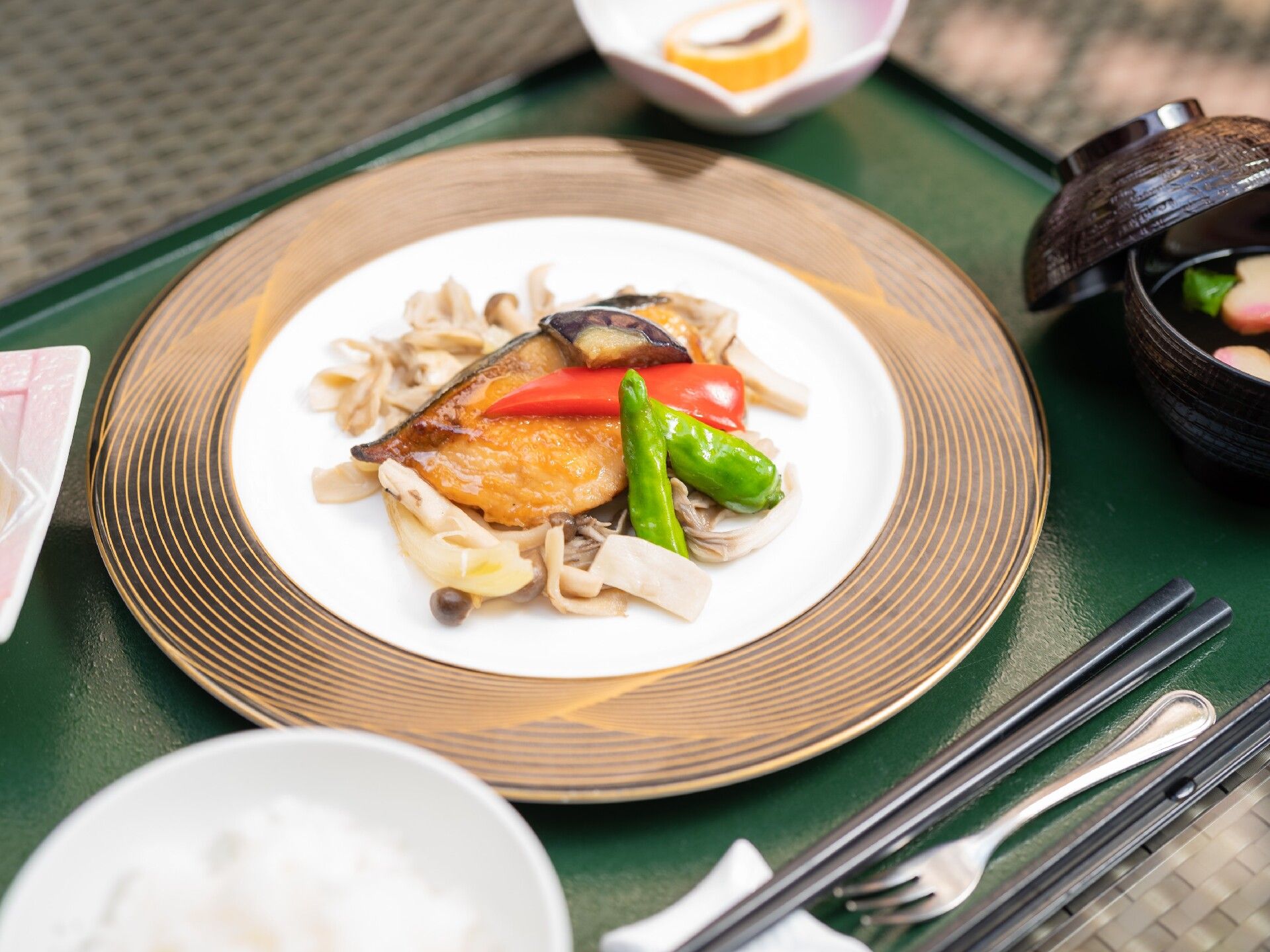 黒いお盆の上には箸置きに置かれた箸やフォークが置かれている。メインの牛丼には白滝がたっぶりと入れられている。お味噌汁、副菜、デザートもある。