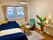 青い寝具がセットされた介護ベッドが置かれたフローリングの部屋には観葉植物やグリーンの一人用の椅子、テーブルなどが置かれている。