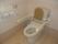 手すりと背もたれが付いたトイレ。壁にはトイレットペーパーホルダーと緑の呼び出しボタンが付き、壁紙はピンクの花柄で家庭的な雰囲気。
