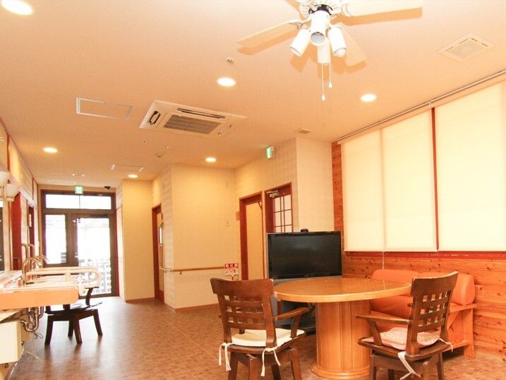手すりが壁に付いた共有スペースにはテレビやテーブルセットがあり、玄関のそばには受付がある。
