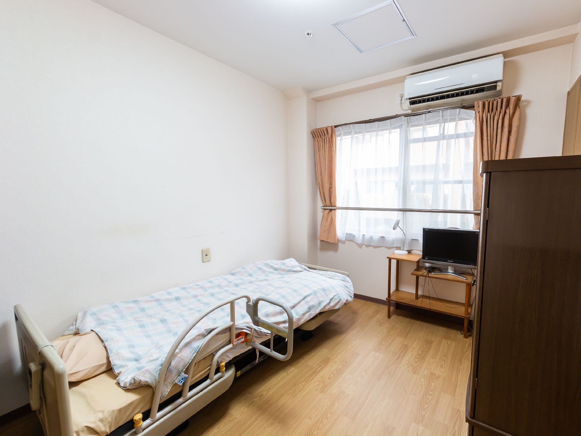 窓から日差しが入り、ベッド、椅子、テレビなどが置かれている居室