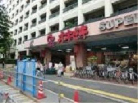 スーパーマーケットの上は大きなマンションである。店舗の前は道路であり、店舗入り口横には自転車がたくさん並んで置かれている。