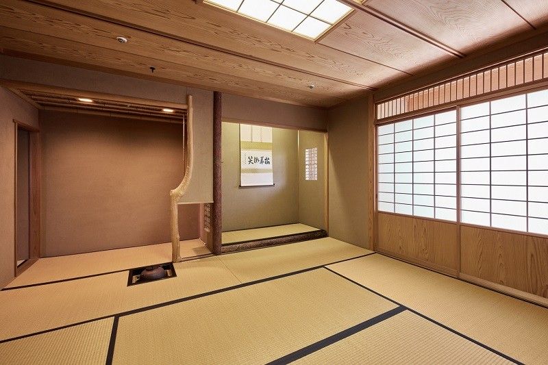 窓際には黒い飾り棚があり、調度品などが置かれている。その並びの壁にはデザイン画が掛けられている。テーブルの上にはバラの花が飾られている。