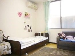 ベッドやエアコン、ソファなどが置いてあるワンルームの様子。小さな一人用の部屋
