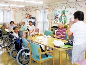 車いすで座っている高齢者と周りにいるスタッフの様子。なにかのレクリレーション時の写真
