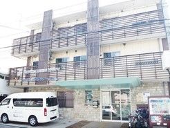 鉄骨造の建物の様子。手前に車がある駐車スペース、スロープ付きの玄関が見えている