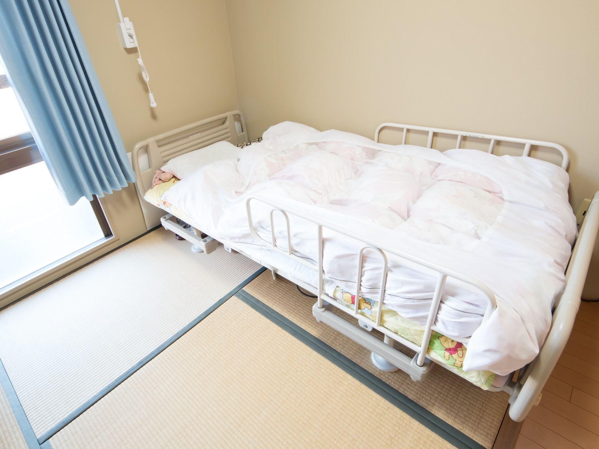 居室は畳が敷かれた和室である。居室のベッドは、入居者様の安全に配慮し、柵を取りつけている。枕元にナースコールがある。