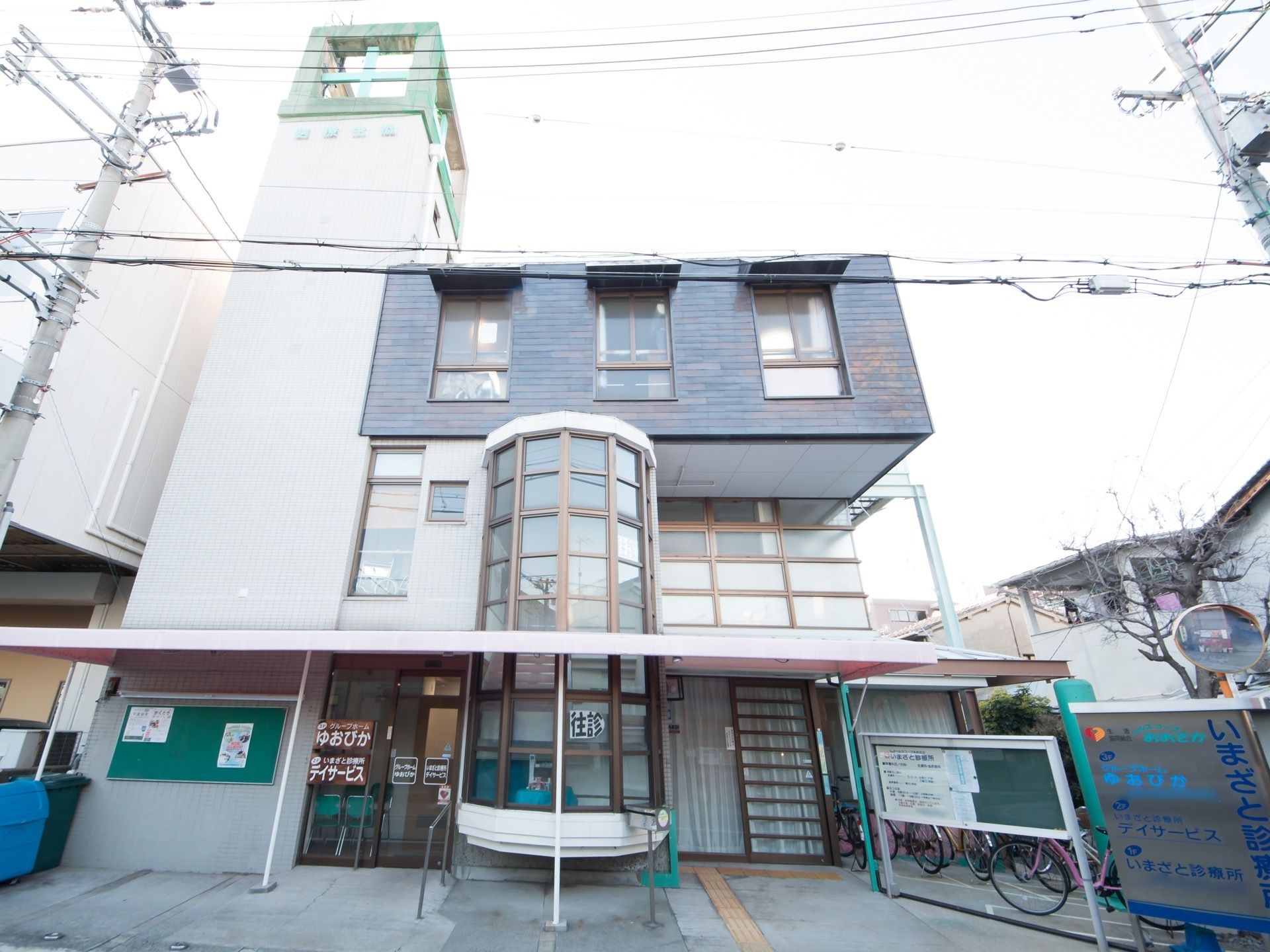 半円形に配置されたガラス窓が特徴的な建物入り口の近くには、手すりを取りつけてある。エントランス付近は段差がないバリアフリー構造である。
