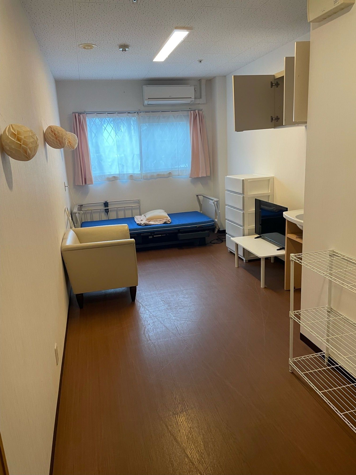 居室の扉は、３枚扉の引き戸である。壁沿いにはベッドが設置され、向かい側の壁際には引き出しとこげ茶色の家具があり上にぬいぐるみが置いてある。