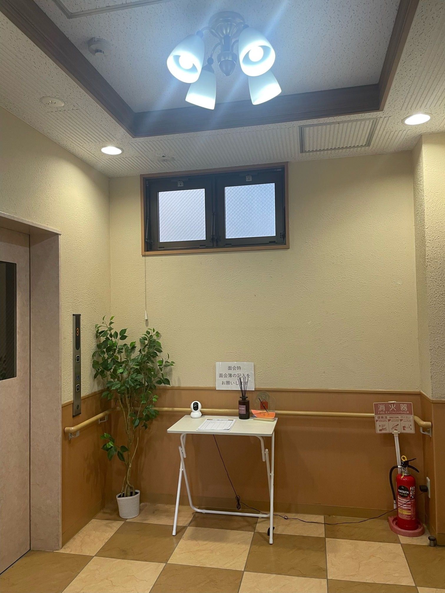 玄関は、ガラス張りの壁面に木目調の扉が付いている。扉の前は、石畳のエントランススペースがあり、床面には緑色のマットが敷かれている。