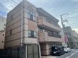 施設の建物は３階建てで、２階と３階に同じ素材同じ形状のベランダが付いている。一見低層マンション風の外観で、建物の端に看板が設置されている。