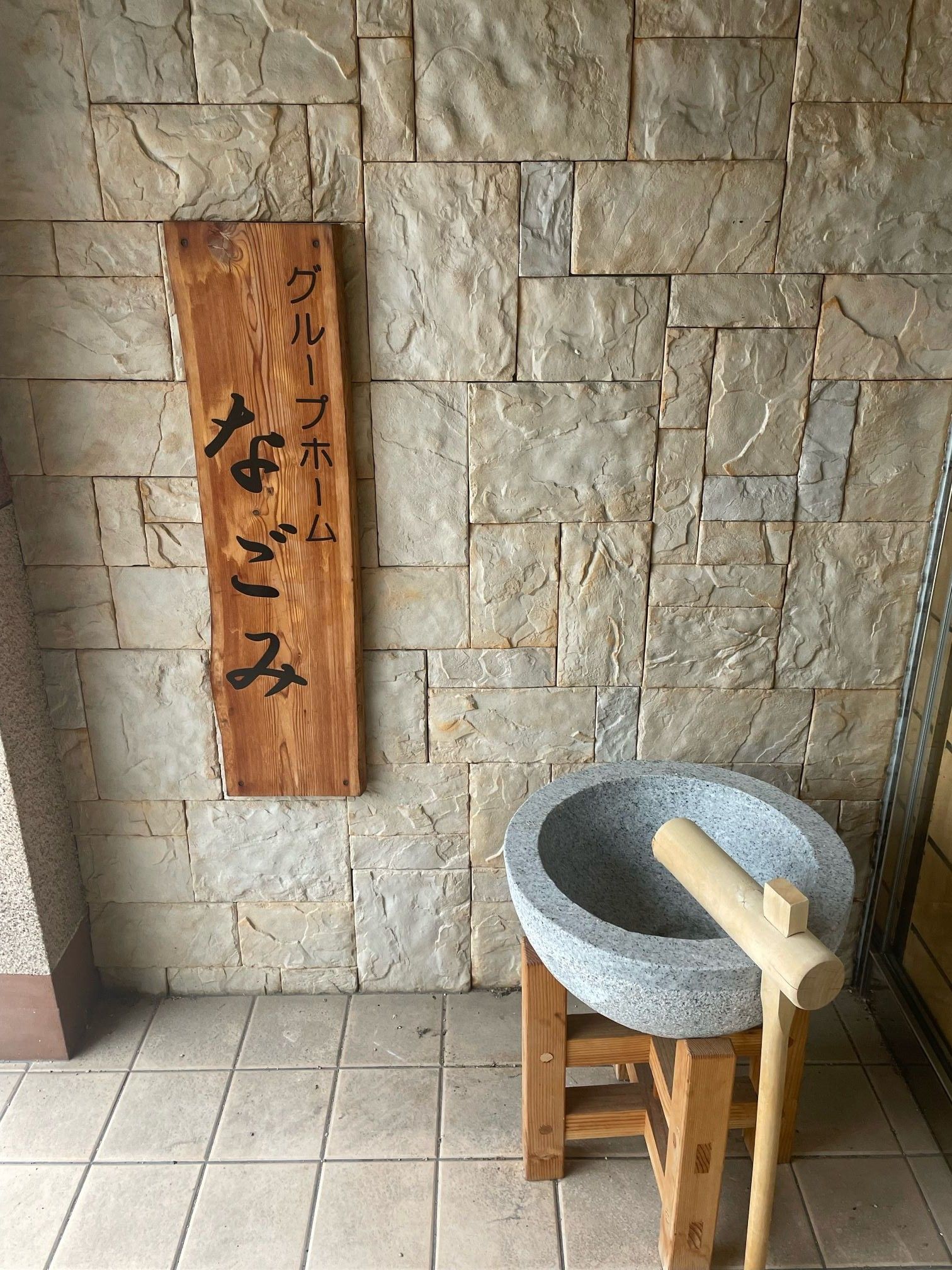 玄関のレンガ調の外壁にはホーム名が書かれた表札と車いすマークのブルーのステッカーが貼られている。