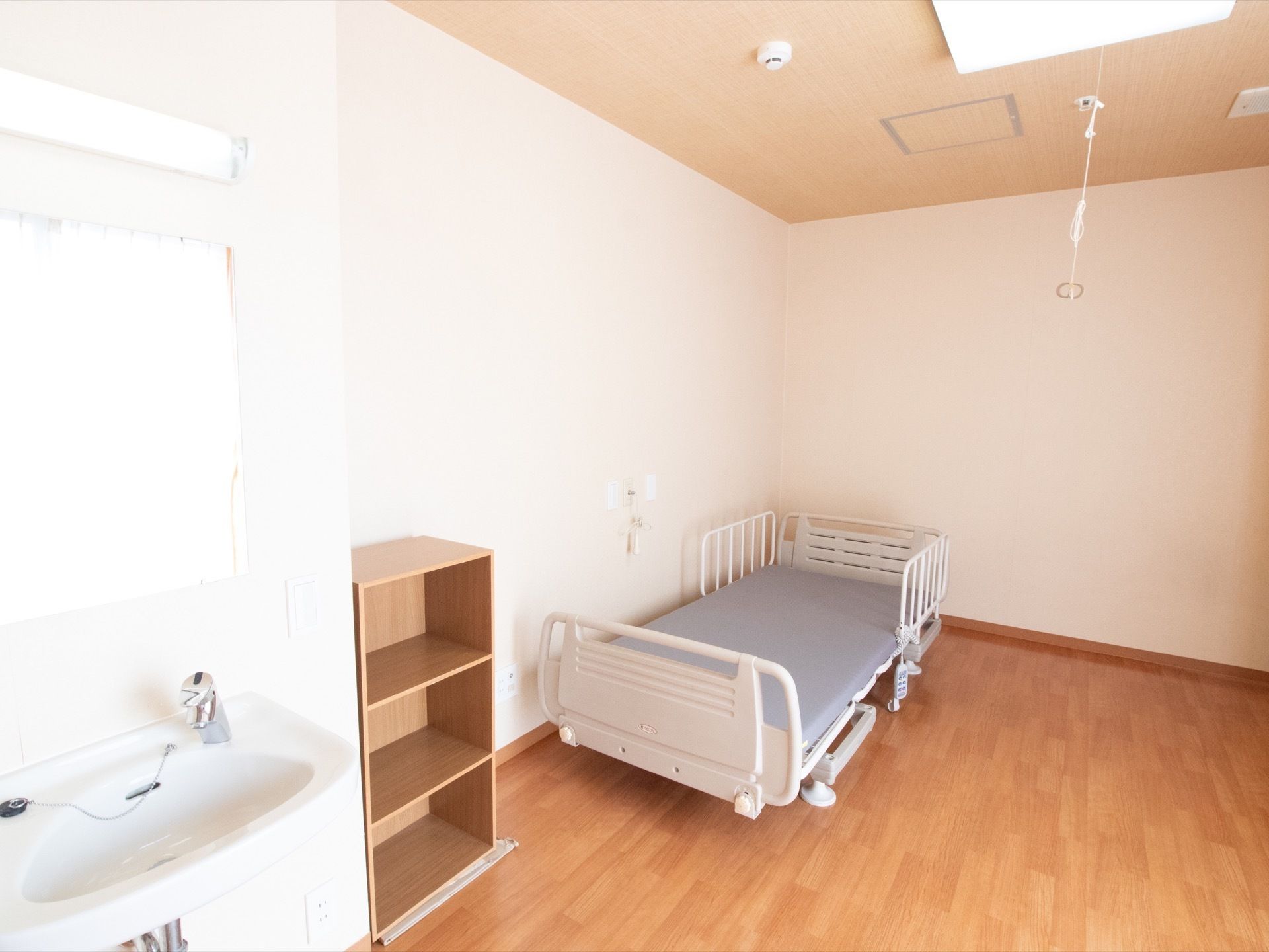 広い間取りの居室である。室内には、照明や洗面台、介護ベッドなど生活に必要な設備が整えられている。ナースコールや火災報知器も設置されている。