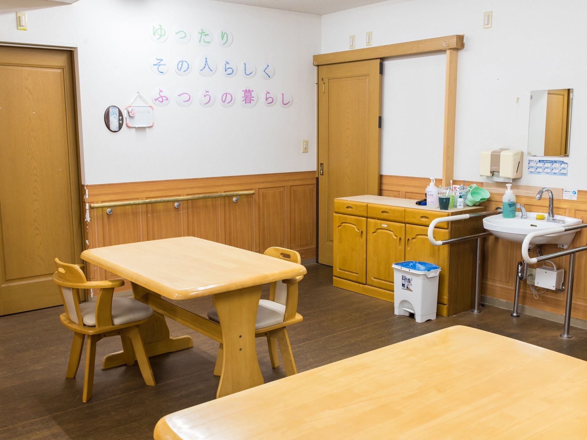 フローリングの床と、下半分が木製になっている白い壁に囲まれた食堂がある。テーブルと椅子が置かれ、扉の側には棚と洗面台がある。